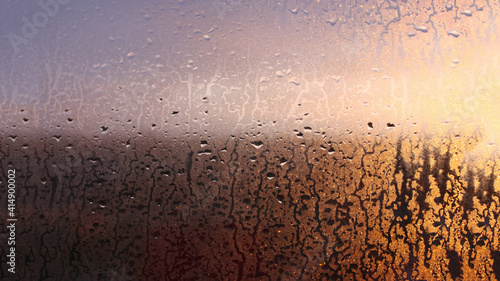 Horizontal natural background with water drops on the window with sunbeams, condensation on the glass with dripping drops