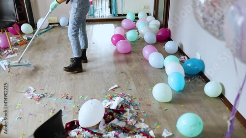 Slow motion, Woman with pushbroom cleaning mess of floor in room after party confetti, morning after party celebration, housework, cleaning service photo