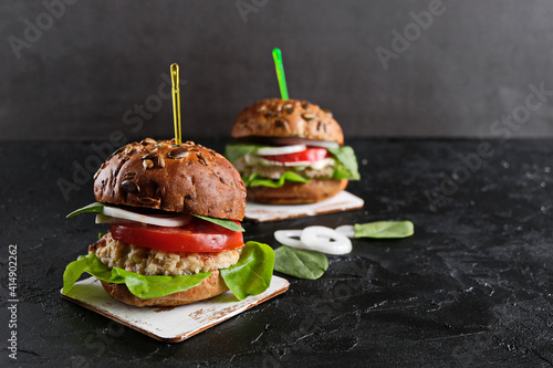 Vegetarian hamburger with tomato, lettuce, onion, bean cutlet and grain bun on dark  background. It  is an alternative to the usual hamburger.  The concept of healthy eating. Copy space.