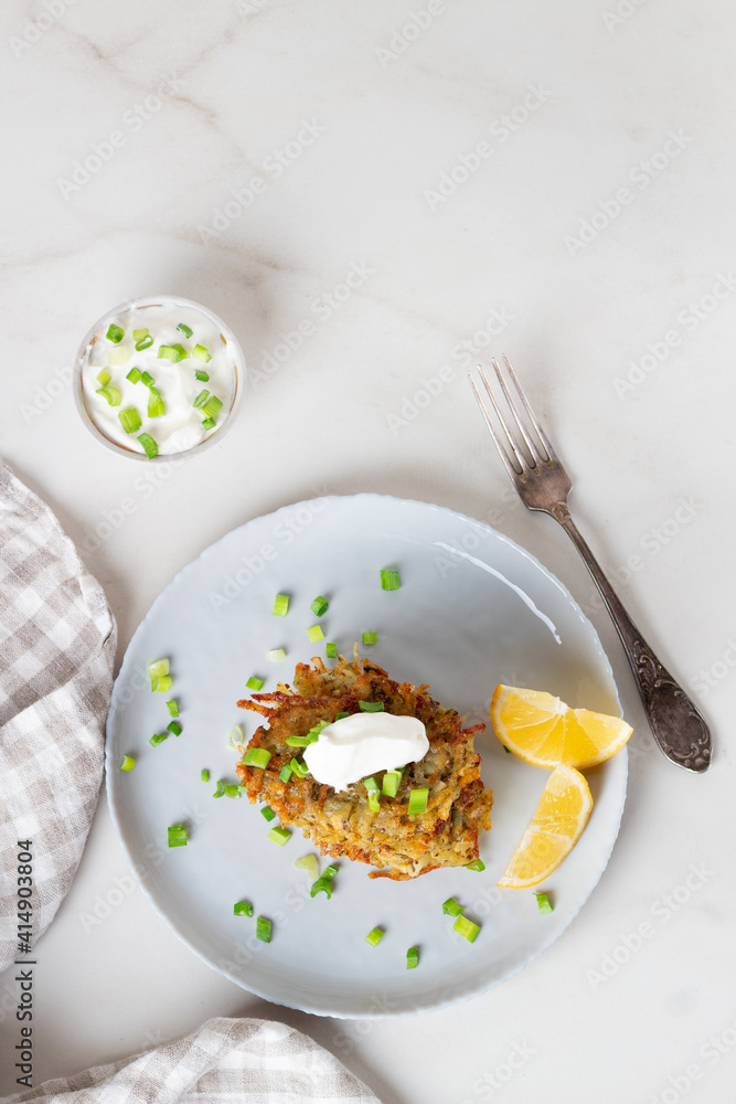 Potato pancakes or draniki with sour cream in plate on marble background. Top view.