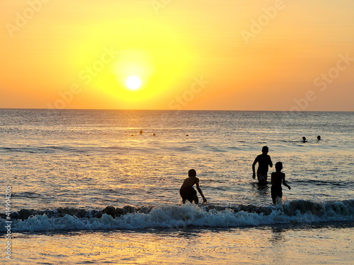Fototapeta Naklejka Na Ścianę i Meble -  Silhouette of kids playing in the ocean at sunset