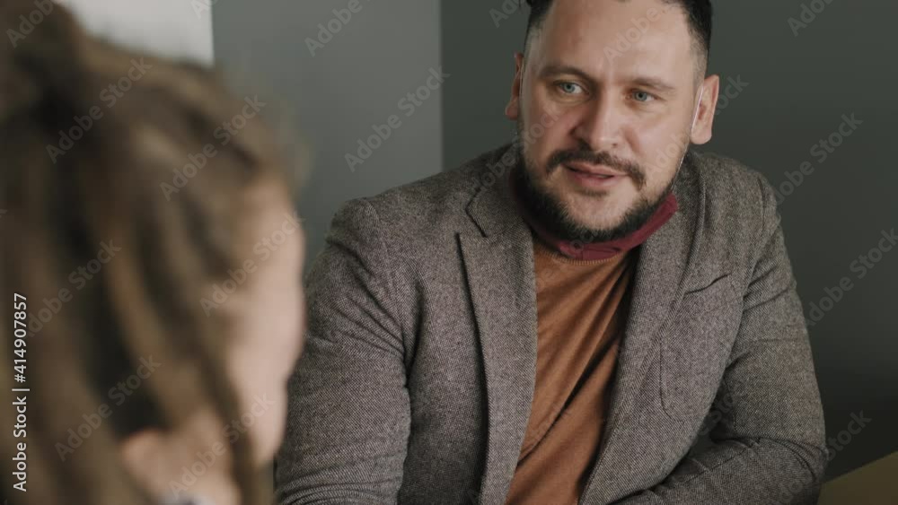 Slowmo tilt up of middle-aged businessman with face mask under his chin chatting with female colleague while having coffee on his break Slowmo tilt up of middle-aged businessman with face mask under his chin chatting with female colleague while having coffee on his break