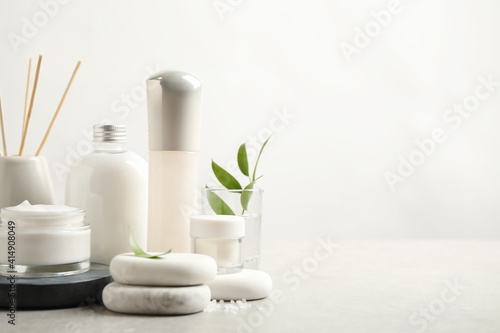 Composition with skin care products and spa stones on light background, space for text