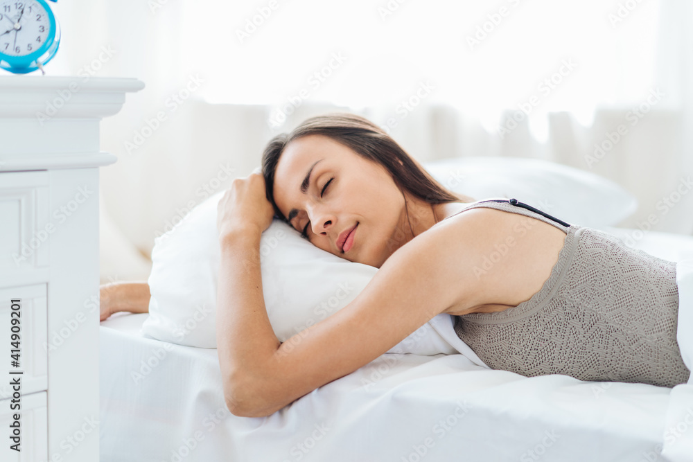 Young pretty woman sleeping in cozy light colored bedroom lying in the bed head on pillow happy and comfortable with eyes closed Young pretty woman sleeping in cozy light colored bedroom lying in the bed head on pillow happy and comfortable with eyes closed
