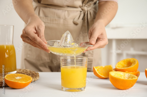 Woman pouring freshly made orange juice in glass at white table, closeup