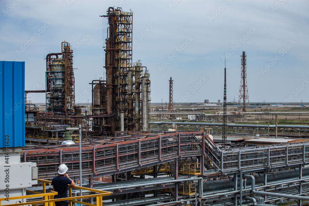 Fototapeta premium Panorama view of oil refinery plant. Distillation columns and pipes. Gas torch masts. Worker in white hardhat on foreground.