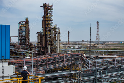 Panorama view of oil refinery plant. Distillation columns and pipes. Gas torch masts. Worker in white hardhat on foreground. © Alexey Rezvykh