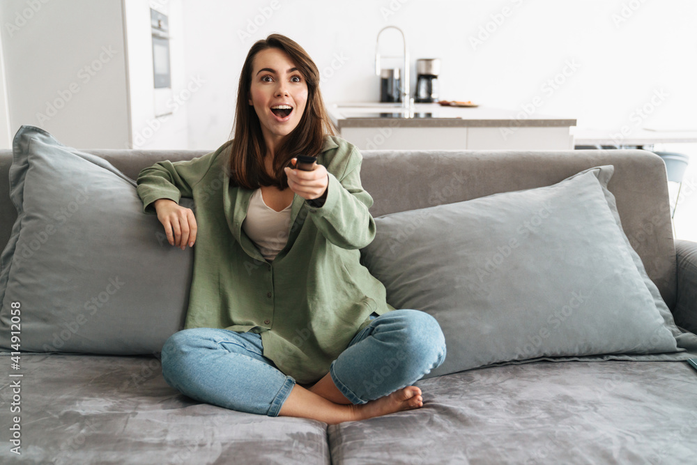 Happy young woman watching tv on sofa - obrazy, fototapety, plakaty 