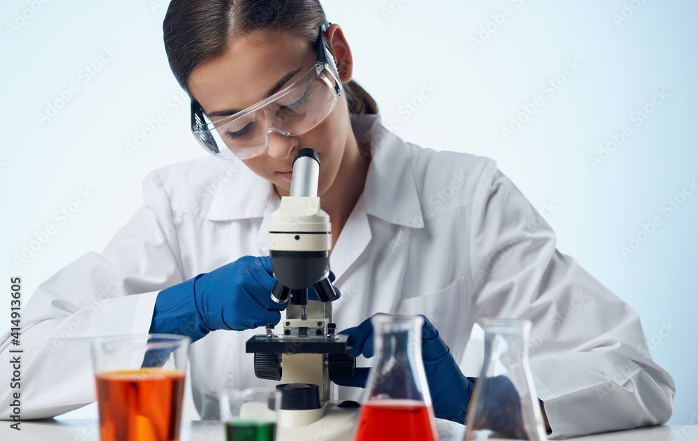 female laboratory assistant with a microscope on the table and glasses on the face liquid in a flask female laboratory assistant with a microscope on the table and glasses on the face liquid in a flask
