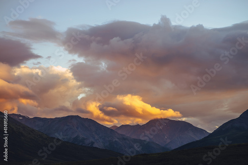 Beautiful mountain scenery with golden dawn light in cloudy sky. Scenic mountain landscape with illuminating color in sunset sky. Silhouettes of mountains on sunrise. Gold illuminating sunlight in sky
