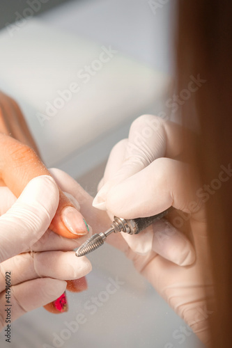 Closeup of manicure master removes nail polish uses an electric nail file in a nail salon