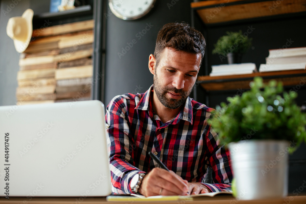 Businessman taking a notes while working on laptop. Young businessman writing in a notebook Businessman taking a notes while working on laptop. Young businessman writing in a notebook