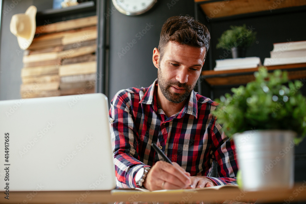 Businessman taking a notes while working on laptop. Young businessman writing in a notebook Businessman taking a notes while working on laptop. Young businessman writing in a notebook