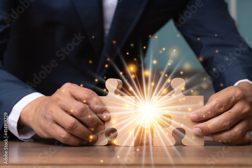 Business man hand connecting jigsaw puzzle on desk with light fair.