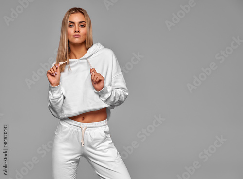 Beautiful sexy blonde woman wear of white set of track suit over gray background photo