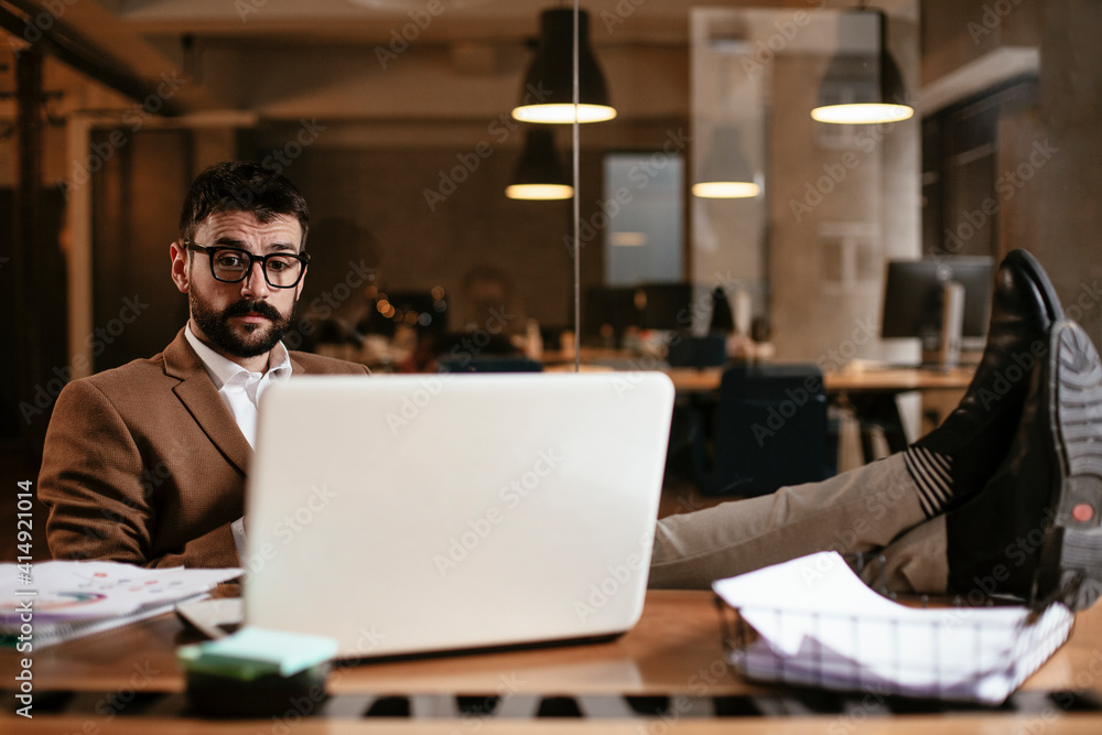 Young businessman working on laptop and drinking coffee in his office. Businessman on coffee break. Young businessman working on laptop and drinking coffee in his office. Businessman on coffee break.