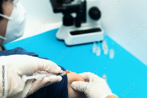Close up of the hands of a doctor with a syringe taking and preparing medicine to vaccinate a child with a mask during the coronavirus pandemic. Defocused background with vaccines and microscope. photo