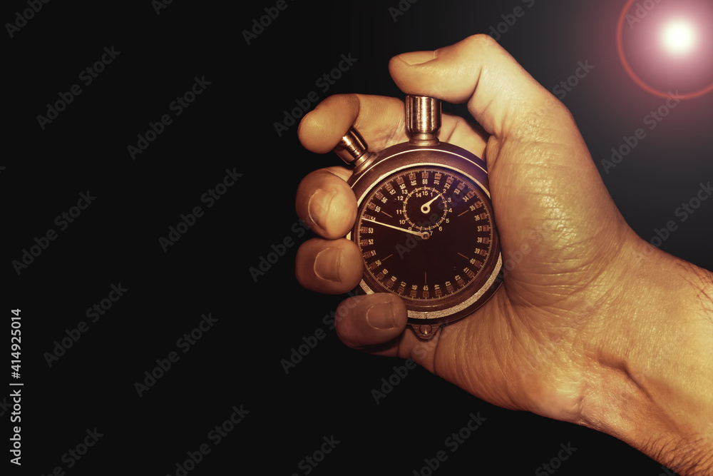 hand with stopwatch on black background with lens flare