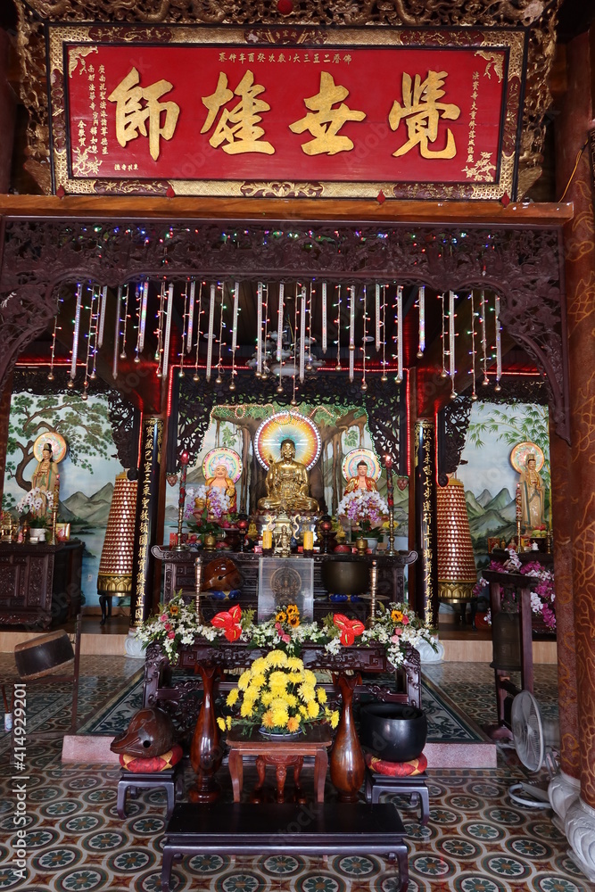 Hoi An, Vietnam, February 18, 2021: Altar with different representations of Buddha in the main hall of the Phap Bao Temple. Hoi An, Vietnam. Vertical view