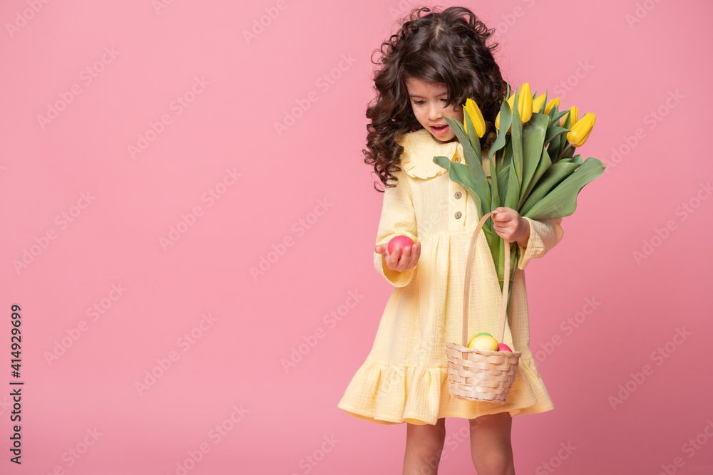 beautiful child girl holding basket with easter eggs and tulips on pink background