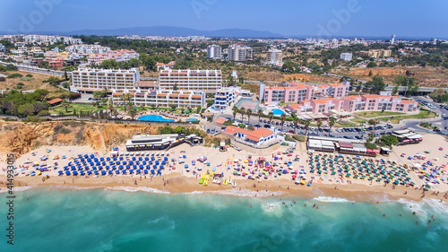Aerial drone shot of a busy beach, amazing cliffs, vegetation and also buidlings in the background. Praia do Vau, Portimao, Portugal.