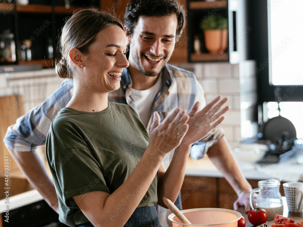 Husband and wife making pancakes at home. Loving couple having fun while preparing food.