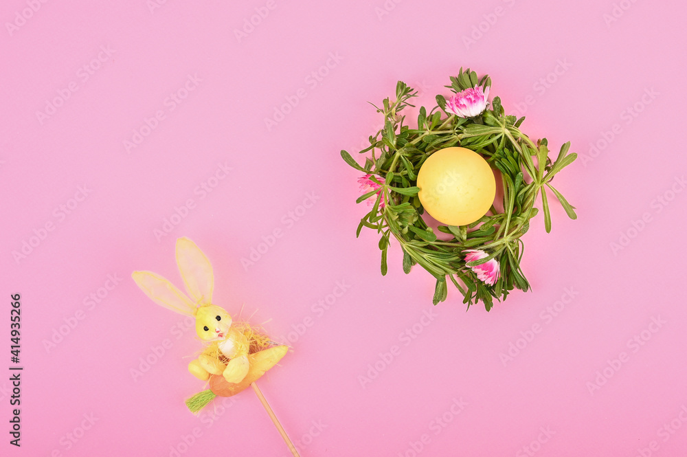 Yellow egg in self-made Easter flower wreath and rabbit toy on pastel backdrop. Easter still life on pink background