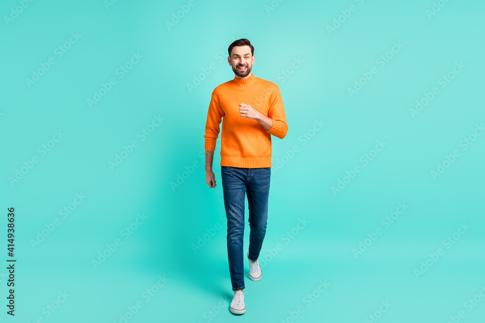 Full size photo of young handsome cheerful man go walk travel wear orange sweater isolated on turquoise color background Full size photo of young handsome cheerful man go walk travel wear orange sweater isolated on turquoise color background