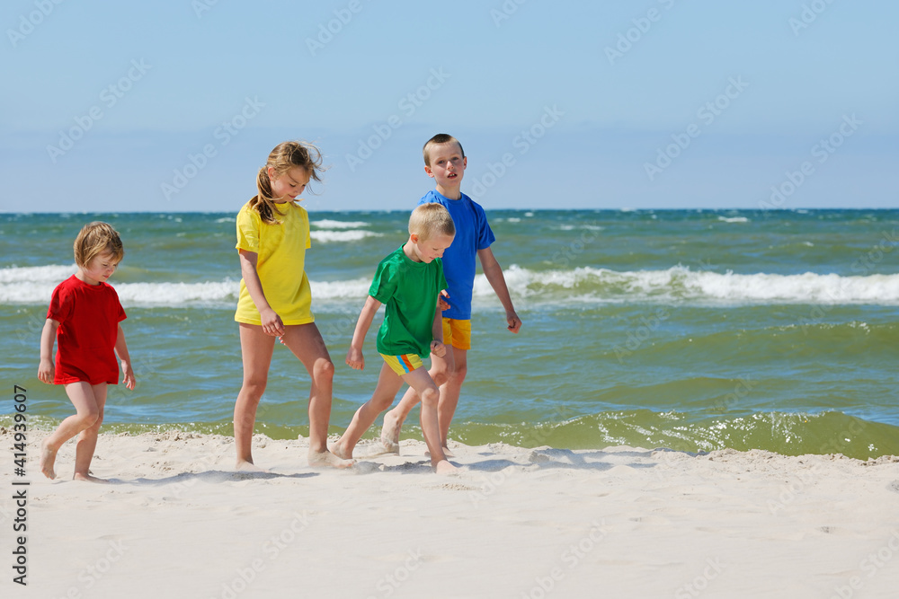Two girls and two boys in colorful t-shirts walking on sandy beach