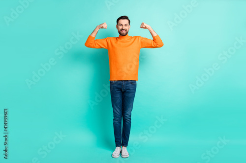 Full size photo of young handsome positive funky smiling man showing muscles biceps isolated on teal color background
