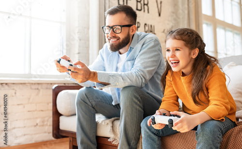 Obraz na plátně father and daughter laugh and play video games together using a video game conso