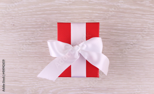 Wooden background with red gift box with white ribbon