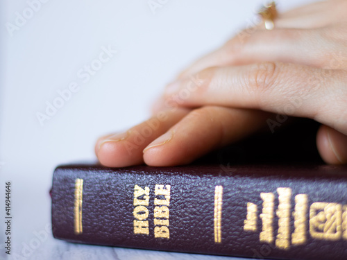Woman praying hand on hand on close Bible with gold letters. Close up of Christian Holy Book. Fervent prayer to God the Father and Lord Jesus Christ. Complete faith and hope in God.