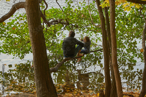 Vater mit Tochter sitzen auf Ast am Schlachtensee, Bäume mit Herbstlaub, Steglitz-Zehlendorf, Berlin, Deutschland