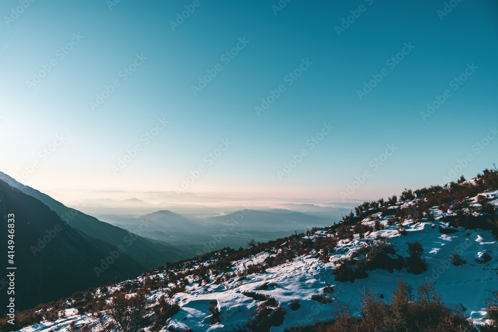 Wide-angle shot of a valley at sunrise with a snow-covered mountain in the foreground