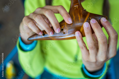 Close-up with the fingers of a young Caucasian woman holding a traditional brown ceramic ocarina in her hands, singing with joy and letting herself be inspired by nature.