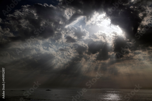 Cloudy sky with a hole and sunbeams over sea