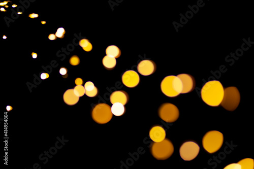 Blurred glowing yellow lights of Christmas garland on black background. Defocus circle bokeh.