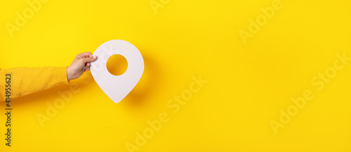 3D location symbol in hand over yellow background, panoramic image photo