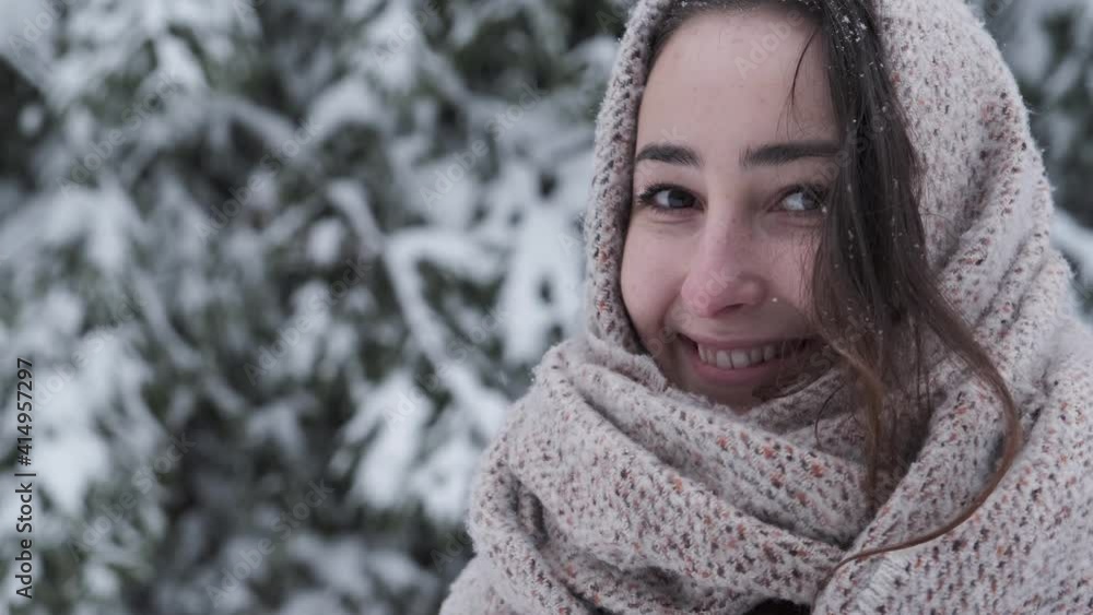Close Up of Young Smiling Beautiful Girl in Winter Clothes Standing in Falling Snowflakes Outside. Portrait of beautiful girl with scarf in the winter forest. Lifestyle, happiness, vacation concept. Close Up of Young Smiling Beautiful Girl in Winter Clothes Standing in Falling Snowflakes Outside. Portrait of beautiful girl with scarf in the winter forest. Lifestyle, happiness, vacation concept.