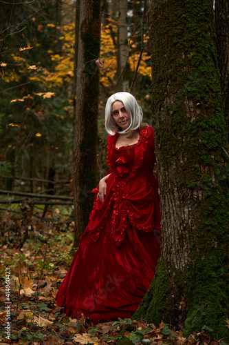 Halloween concept  glamorous costume detail. Young beautiful and mysterious woman in woods  in white Dress and Red Cloak. Little red hood or vampire story