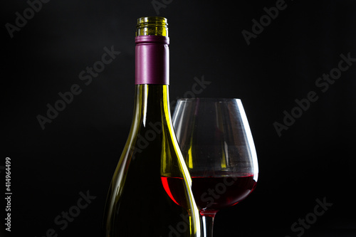 Wine bottle and glass with red wine on dark glossy background.