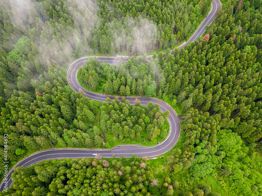 Winding road through the forest, from high mountain pass, in summer time. Aerial view by drone. Romania - obrazy, fototapety, plakaty 