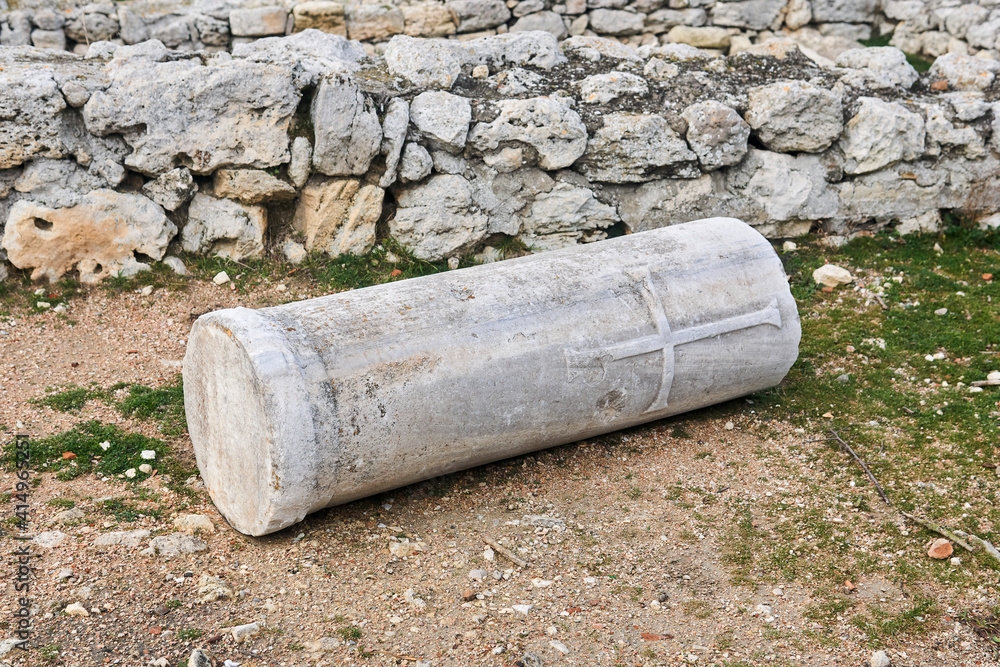 fragment of an antique column with a christian cross carved on it, lying among the ancient ruins