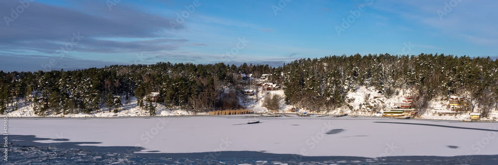 Beautiful view of the northern snow covered coast of the Baltic sea in winter day. Panorama of the shores of Scandinavia Sweden or Finland from cruise ship. Forestry islands on the horizon. Header.