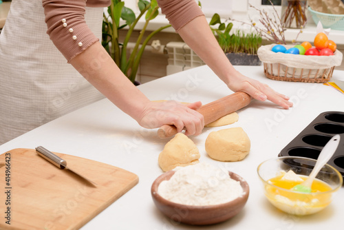 the process of rolling out the dough at home on the table is the hands of a woman for making cruffins festive pastries for Easter . side view of a bright kitchen , with painted eggs