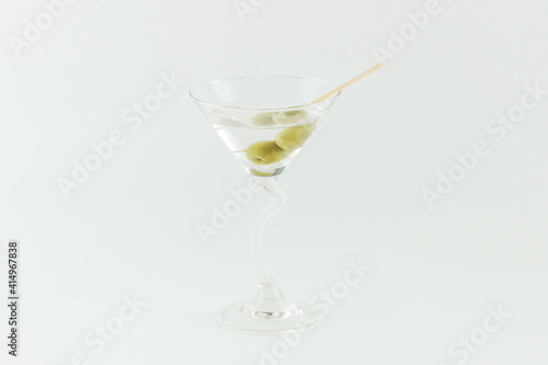 Martini cocktail with green olives on white background