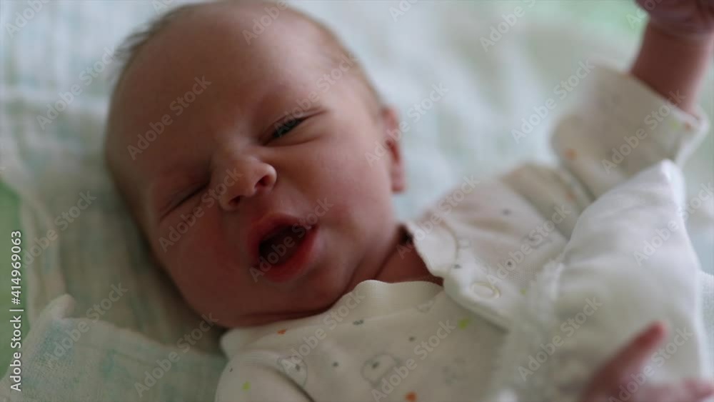 New born baby boy resting in bed exploring his hands and the world around him New born baby boy resting in bed exploring his hands and the world around him