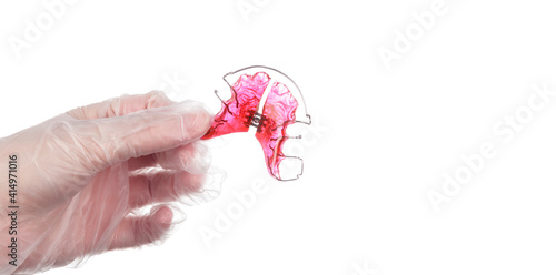An orthodontist wearing disposable gloves shows an orthodontic appliance for children on white background with copy space