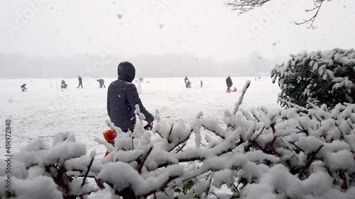 Happy family with children sleigh, bob in winter city park UK in snow fall. 4k